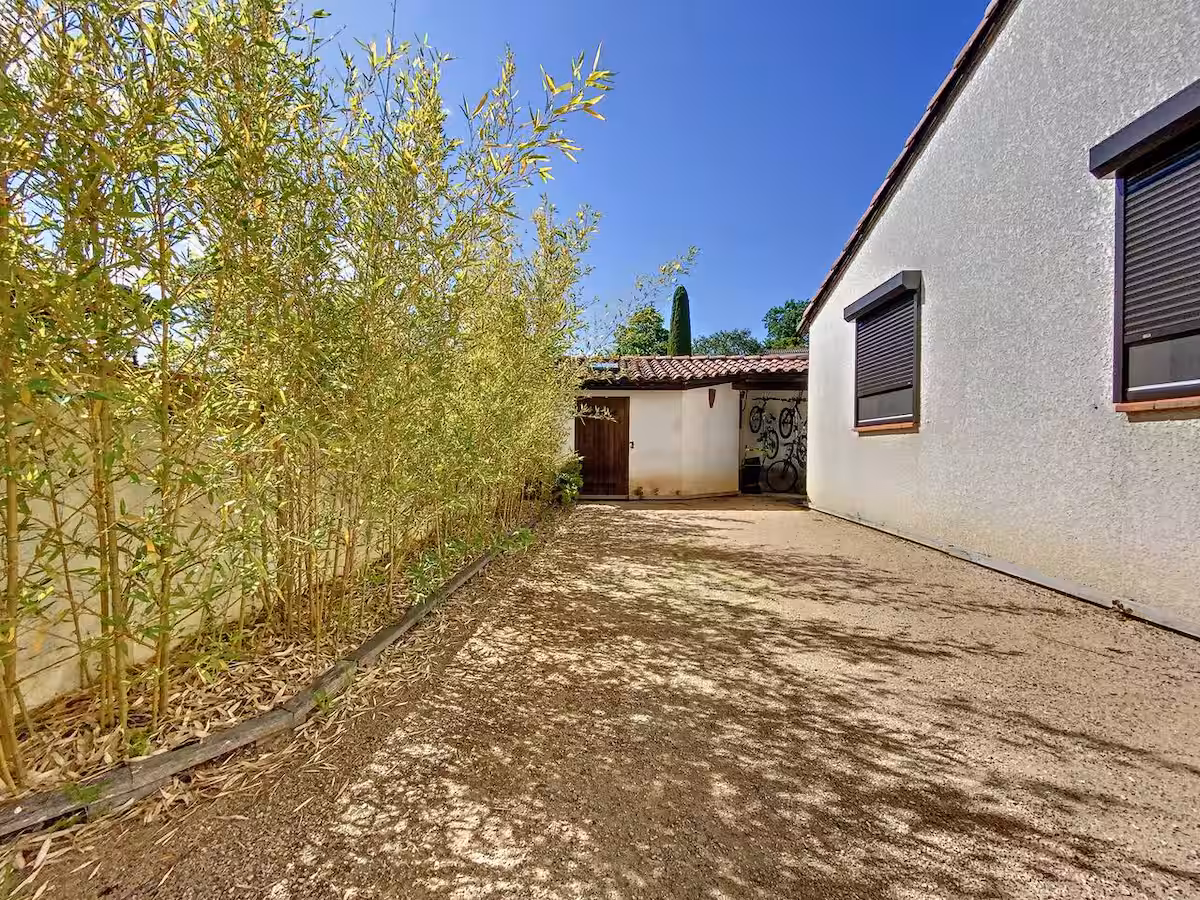 Petanque court with bamboo on left and hose on right. Pool house in background.