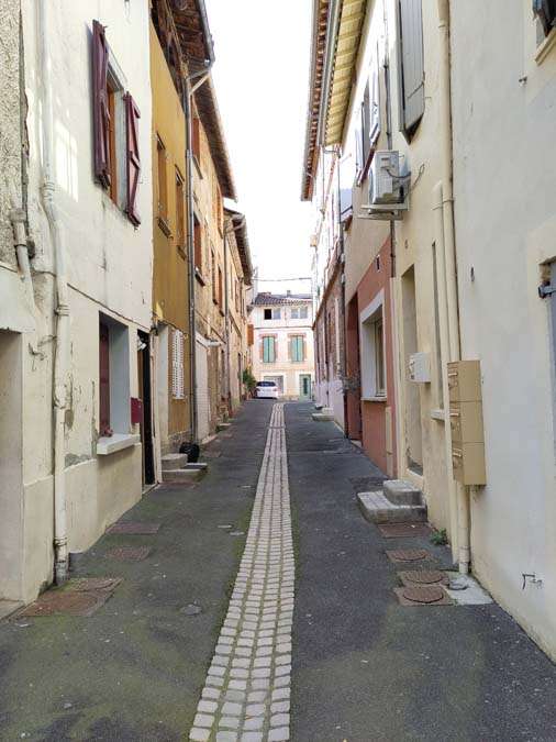 Cobbled street with drain in middle and two story houses