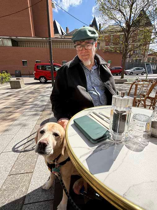 Older man looks at yellow lab at cafe table